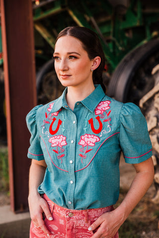 Close view of the Rose Frontier Top highlighting gathered puff shoulders, pink sleeve piping and floral horseshoe embroidery.