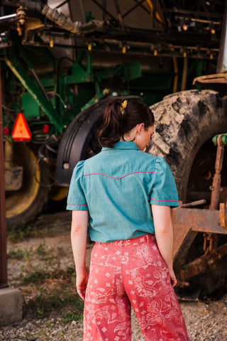 Back view of the teal Rose Frontier Top, showing pink piping along the Western yoke and short puff sleeves.