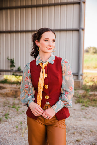 Sage Paisley Blouse with a pointed collar and sheer printed sleeves, styled beneath a burgundy vest with a yellow tie.