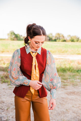 Model adjusting the Sage Paisley Blouse sleeve, showing its sheer balloon shape, colorful paisley pattern and fitted cuff.