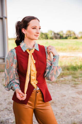 Model wearing the Sage Paisley Blouse by Turquoise Haven with gathered sleeves, a burgundy vest and a yellow patterned scarf.