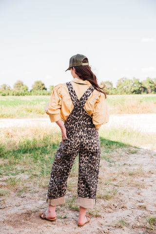 Back view of the Savannah leopard print barrel-leg jumpsuit showing crossed straps, rear patch pockets, and rolled cuffs.