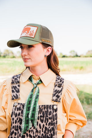 Close-up of the Savannah leopard print jumpsuit showing adjustable buckle straps and a bib pocket with a green scarf.