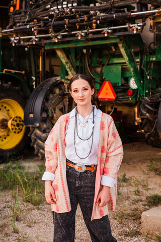Sedona Ruffle Tie Top in White layered under a pink patterned cardigan with black jeans, a Western belt and long necklaces.