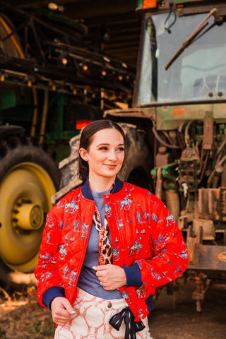 Southern Cowboy red bomber jacket worn open over a blue-gray top with a patterned neck scarf and cream rope-print pants.