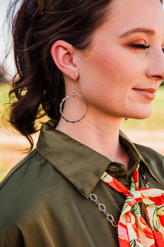 Stamped Dangle Hoop Earring worn on the ear, showing its circular silver-tone shape beside an olive collar and citrus scarf.