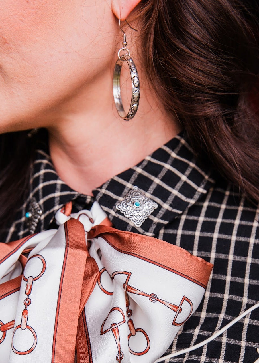 Close-up of a West & Co stamped dangle hoop earring, showing silver-tone patterned metal and a fishhook ear wire.