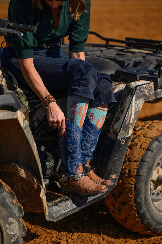 Person sitting on an ATV wearing blue jeans and cowboy boots with a colorful pattern.