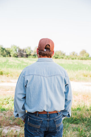 Rear view of the tan Roost Logo Trucker Hat showing brown mesh panels and an adjustable snapback closure on a model.