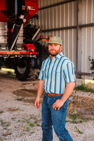 Angled view of the Tristan blue striped short sleeve pearl snap shirt, worn tucked into jeans with a tooled brown belt.