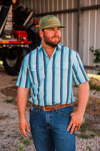Tristan blue striped short sleeve pearl snap shirt with a pointed collar and Western chest yokes, worn with a brown belt.