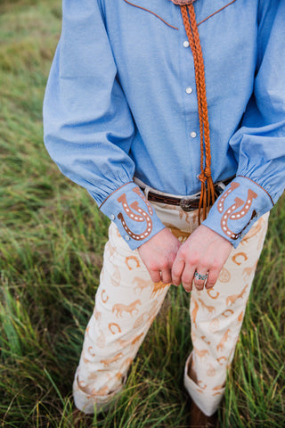 Close-up of tan horseshoe embroidery on the chambray cuffs of the Turquoise Haven Lucky Trails blouse, with pearl-snap details.