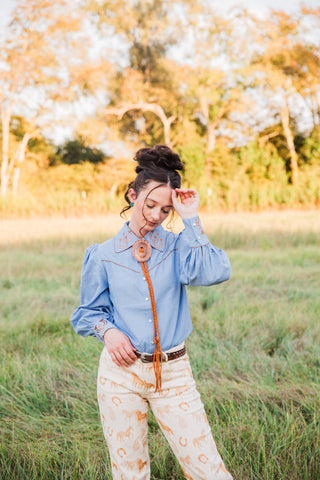 Lucky Trails Horseshoe Blouse by Turquoise Haven with a raised sleeve showing pearl-snap cuffs and gathered chambray fabric.