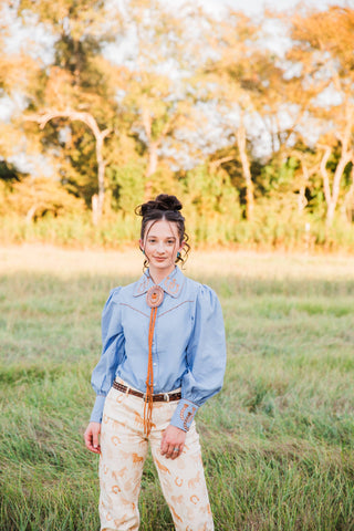 Turquoise Haven Lucky Trails Horseshoe Blouse in chambray blue, front view with embroidered collar, puff sleeves and pearl snaps.