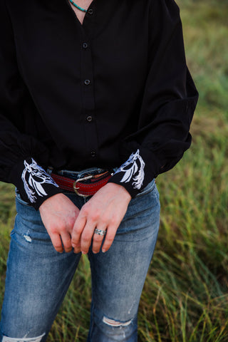 Close-up of white horse embroidery on both black cuffs of the Turquoise Haven Midnight Rider blouse, styled with blue jeans.