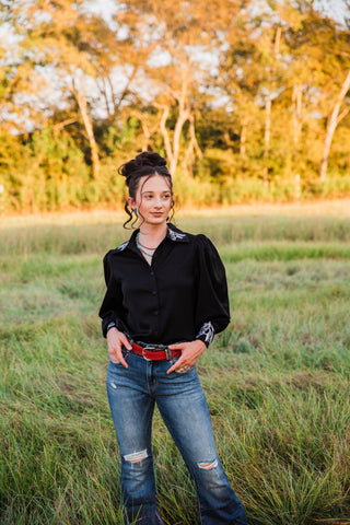 Midnight Rider Horse Embroidered Blouse by Turquoise Haven tucked into blue jeans, with white horse details and puff sleeves.