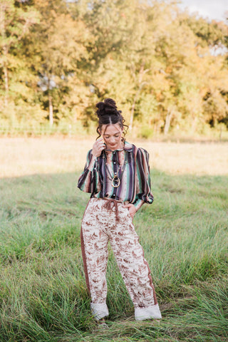 Sagebrush Trails Serape Blouse by Turquoise Haven tucked into ranch-print jeans, with green stripes and layered necklaces.