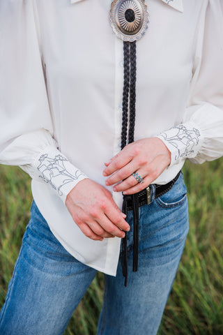 Turquoise Haven Wild Rein blouse cuff close-up showing dark bucking horse embroidery on white cuffs and gathered sleeves.