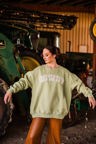 Sadie wearing size S/M in the green HOWDY sweatshirt with arms extended, showing its oversized width, long sleeves, and ribbed hem.