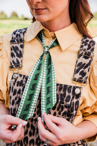 Close-up of the green Hereford Twilly showing cattle motifs, gingham edging, and pointed ends held over leopard overalls.