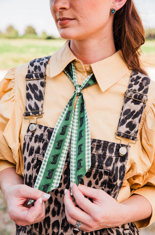 West & Co Hereford Twilly tied at a tan shirt collar, showing green cattle print and gingham borders in close-up.