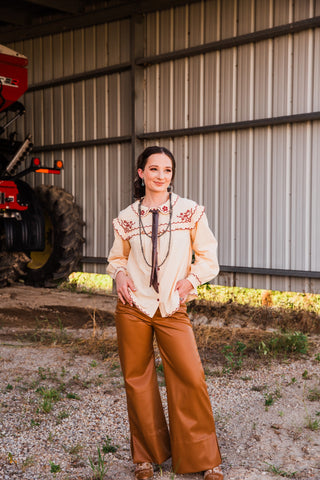 Winchester Top worn untucked, showing the cream button front, burgundy scalloped trim and gathered cuffs with tan pants.