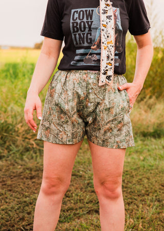 Women’s camo boxer shorts showing a relaxed leg opening and side pocket, paired with a tucked-in black graphic tee.