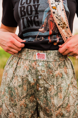 Close-up of women’s camo boxer shorts showing the elastic waistband, Howdy Hanny label, three white buttons and woodland print.