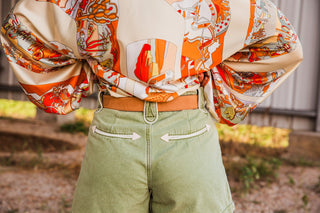 Wrangler Mommy + Me Belt viewed from behind, showing the tan strap across olive shorts beneath a tucked Western print blouse.