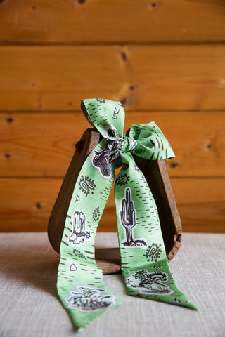 XOXO Art & Co 1940’s Cowboy green silk twilly showing cactus and cowboy artwork, paisley accents and long pointed tails.