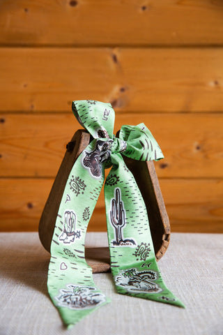 1940’s Cowboy silk twilly by XOXO Art & Co tied in a bow, with green fabric, cactus illustrations and vintage western motifs.
