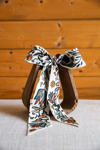 Ink in Bloom silk twilly by XOXO Art & Co tied in a bow, with colorful flowers and bold black outlines on ivory fabric.