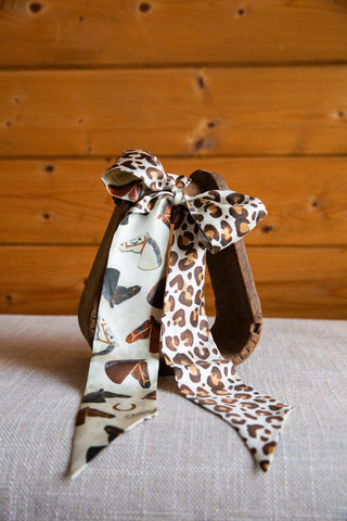 Wild Horses silk twilly by XOXO Art & Co tied in a bow, showing horse portraits on cream and contrasting brown leopard print.